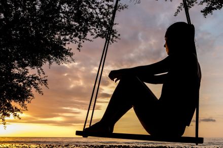 A serene sunset silhouette of a woman sitting on a swing by the seashore, evoking tranquility and reflection.