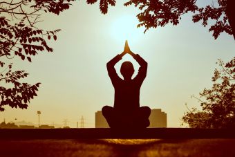 Silhouette of a person practicing yoga outdoors during sunrise, creating a calming atmosphere.